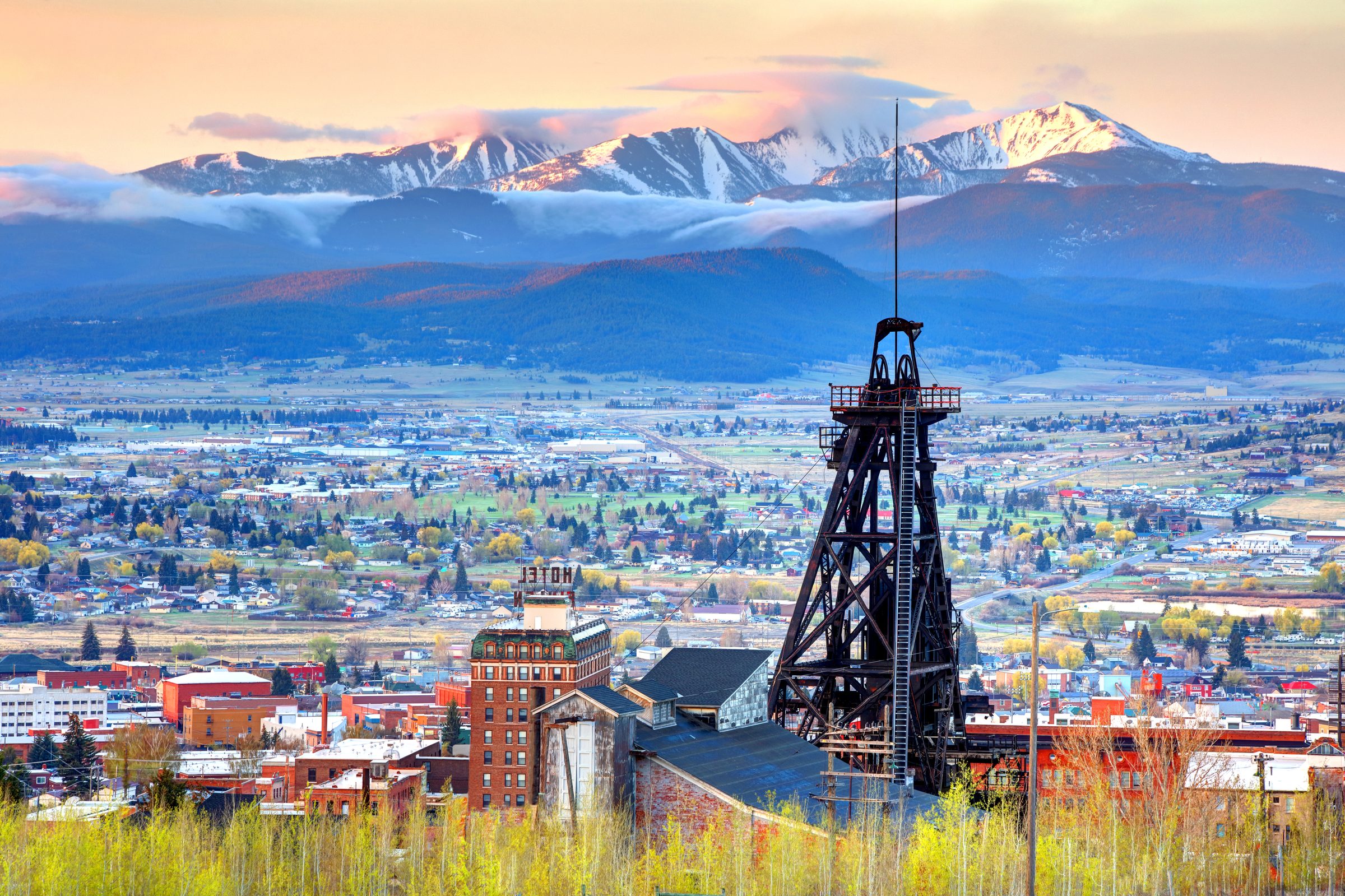 A Butte headframe above uptown at sunset, with the snow-capped Highland Mountains beyond