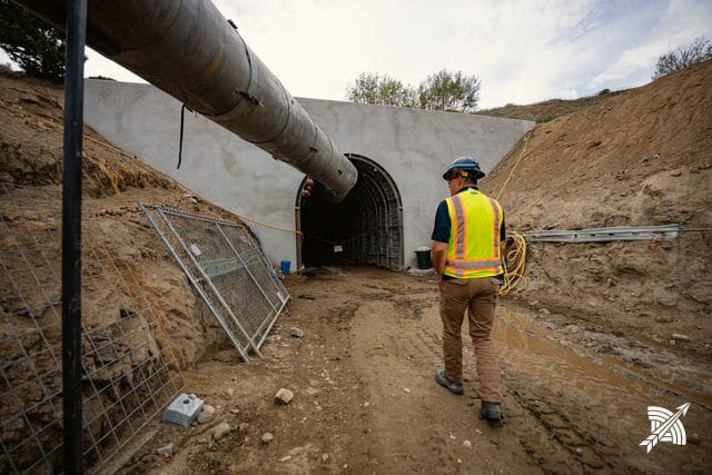 A worker in hi-vis walking toward the portal arch, ventilation duct overhead